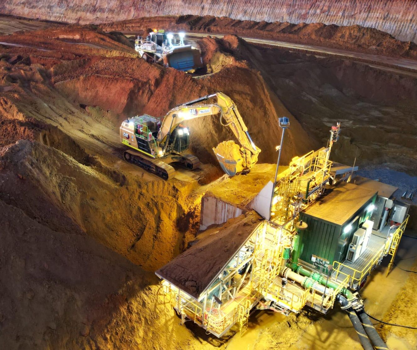 Excavator and mining equipment operating at night within an open-cut mine.